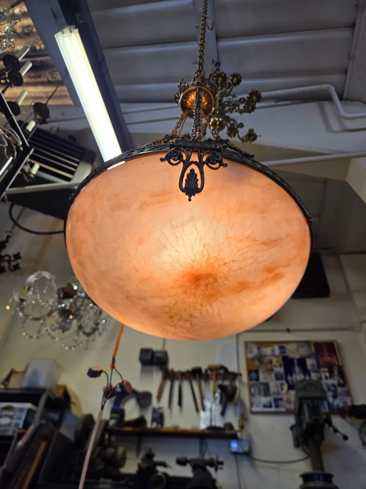 Alabaster bowl chandelier viewed from below and illuminated during testing in the workshop, showing natural veining in the stone.