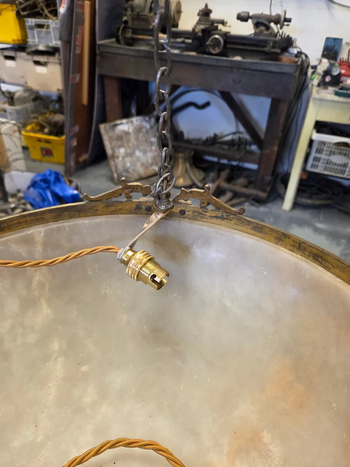 Close view of a new brass light holder fixed to the inside rim of an alabaster bowl on a small bracket, with twisted fabric-covered cable running across the interior.