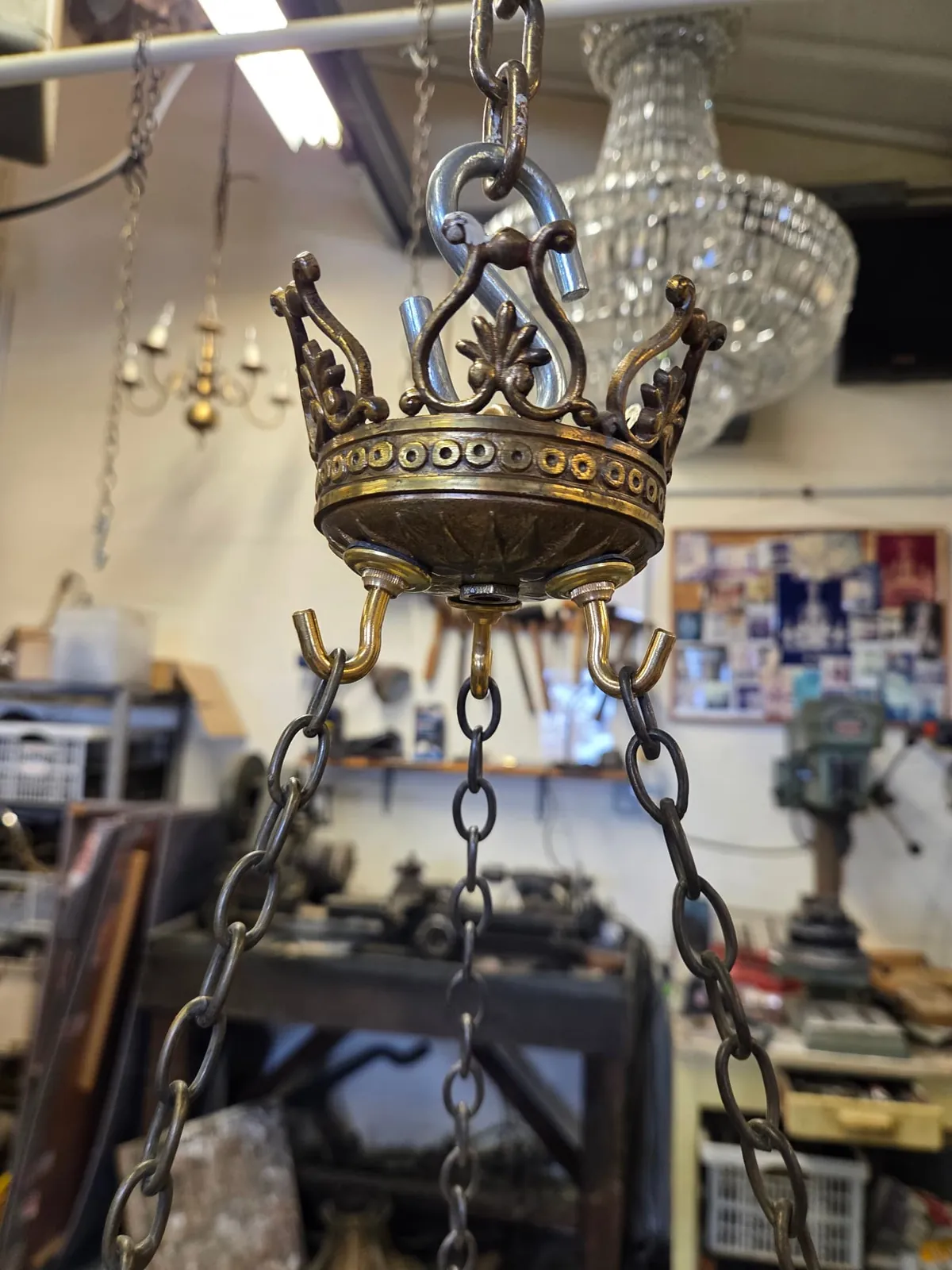 Decorative brass crown of an alabaster chandelier with three new hooks and suspension chains, hung in the G & P Cohn workshop during rewiring.