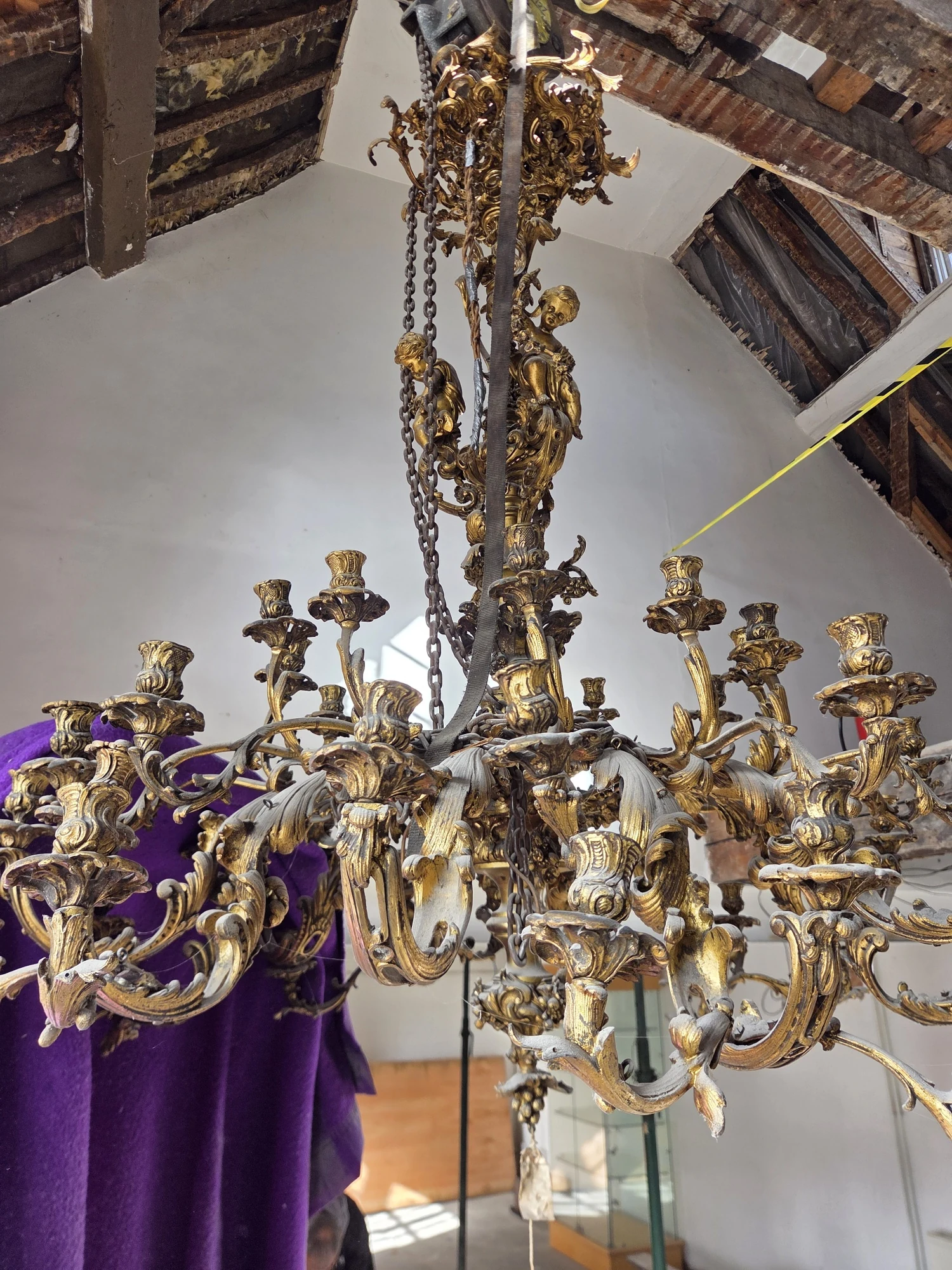 Large 44-light gilt Rococo-style chandelier hanging from a timber beam in an outbuilding in Wallingford before dismantling.