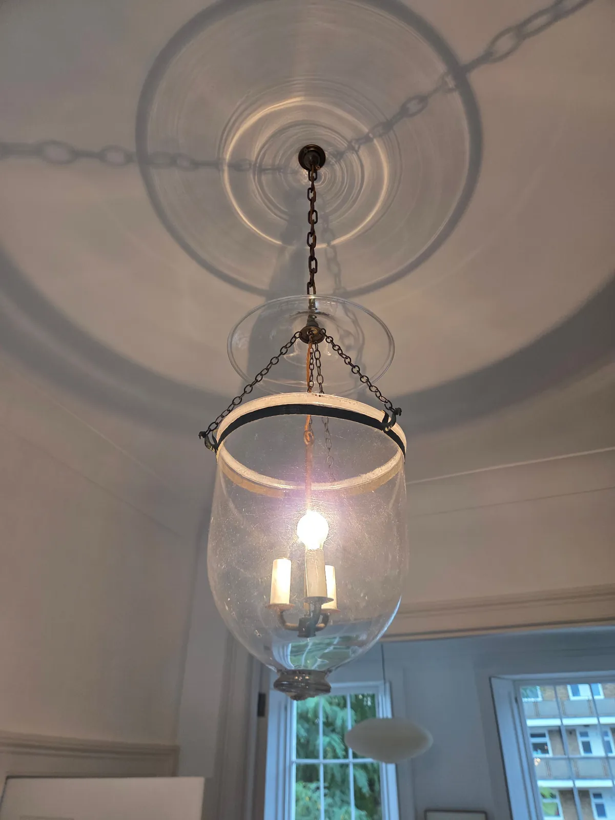Glass bell lantern viewed from below, showing the glass jar, smoke cap and chain suspension at a property in Camden, London.