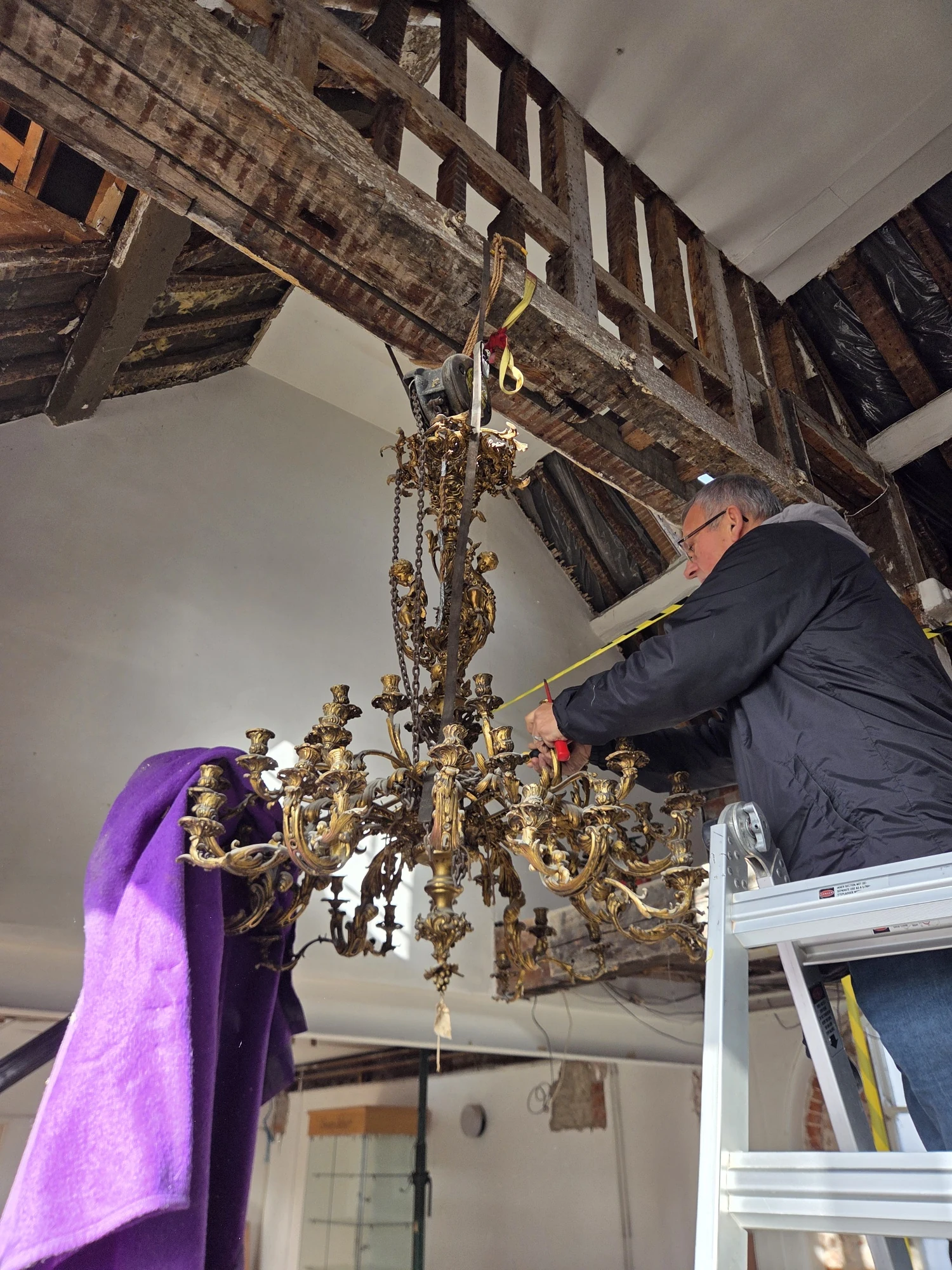 G & P Cohn working from a ladder to remove arms from the suspended Rococo chandelier.
