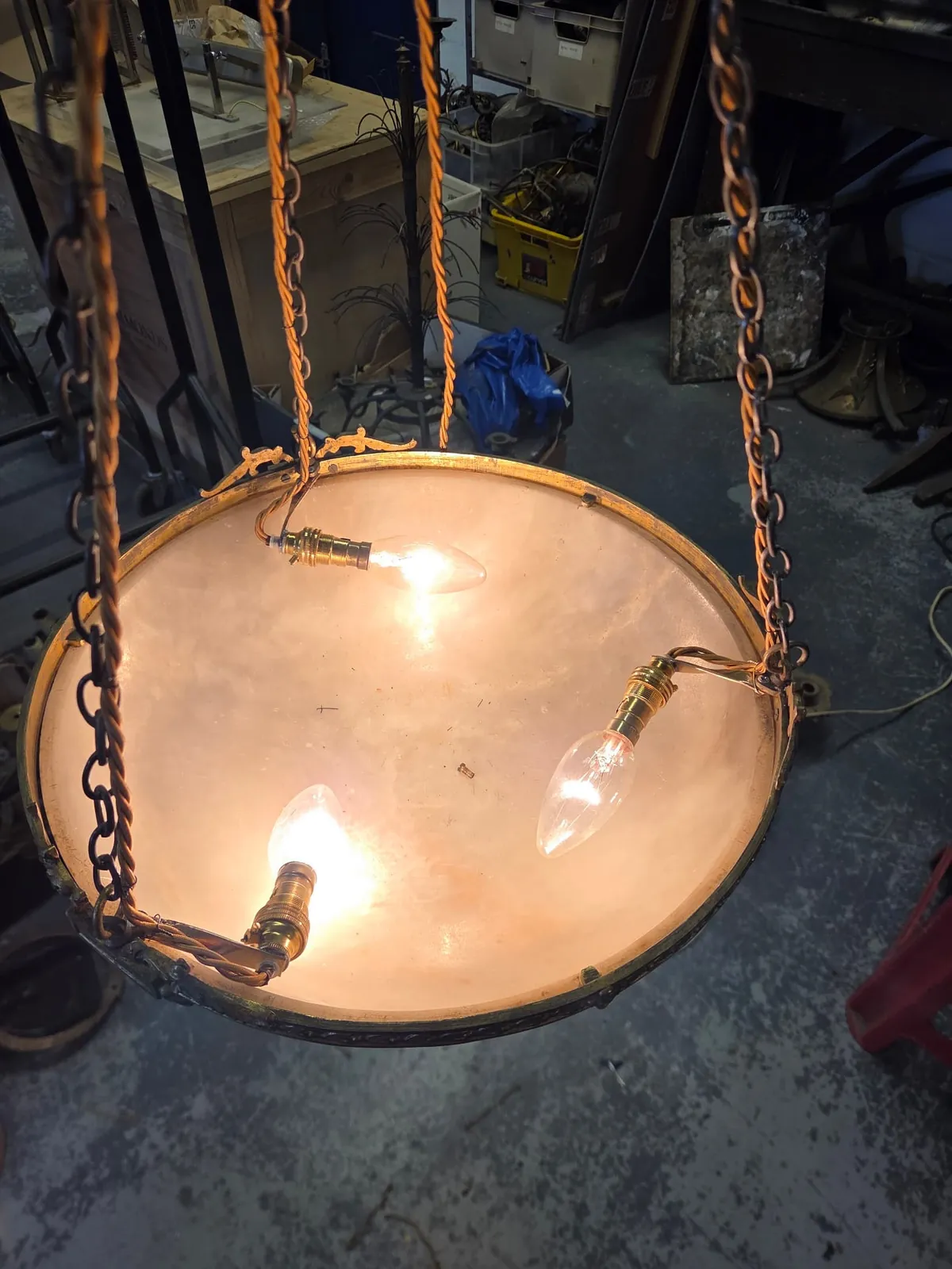 Top-down view inside an alabaster bowl showing three brass light holders with candle-shaped bulbs lit and fabric-covered cable routed alongside the suspension chains.