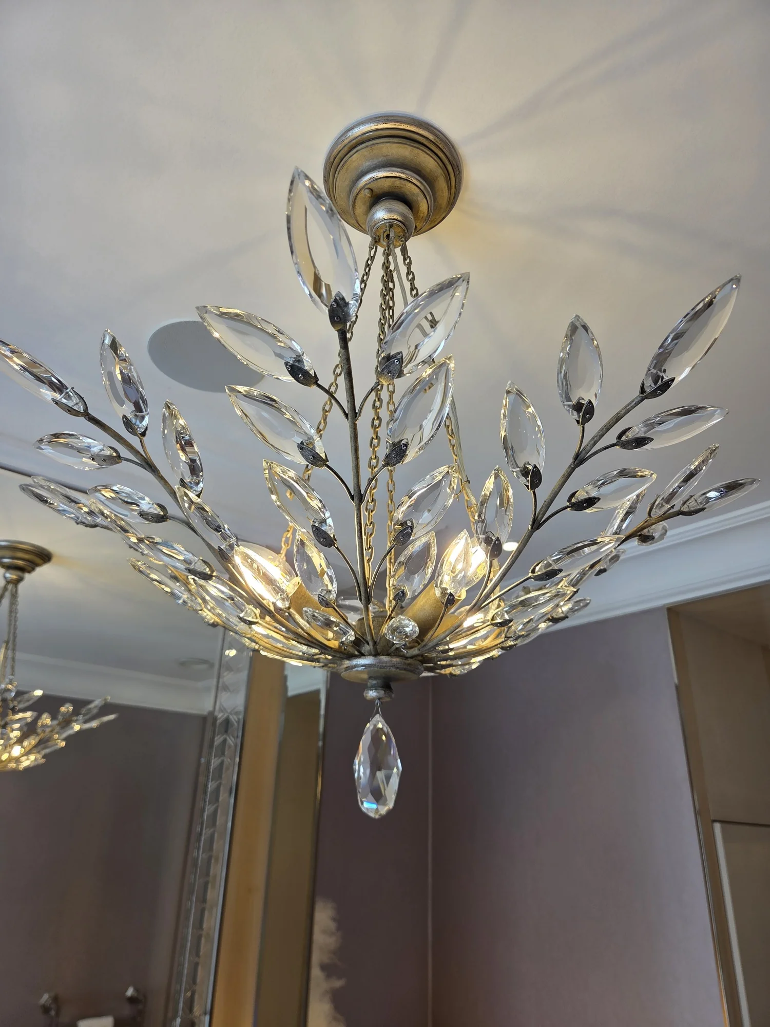 Decorative metal framework and glass leaves of an illuminated chandelier beneath its ceiling rose in The Boltons.
