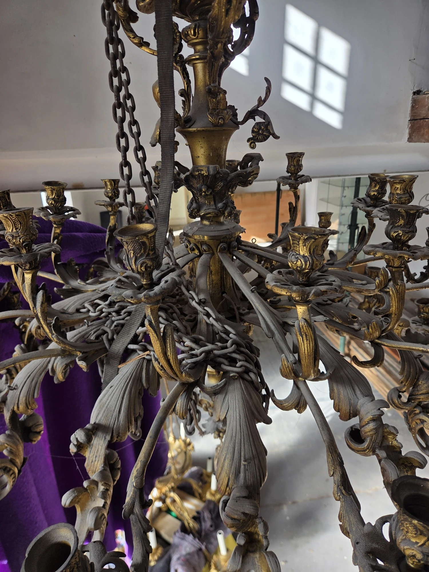 View up into the gilt chandelier showing its many scrolling arms and candle holders around the central stem.