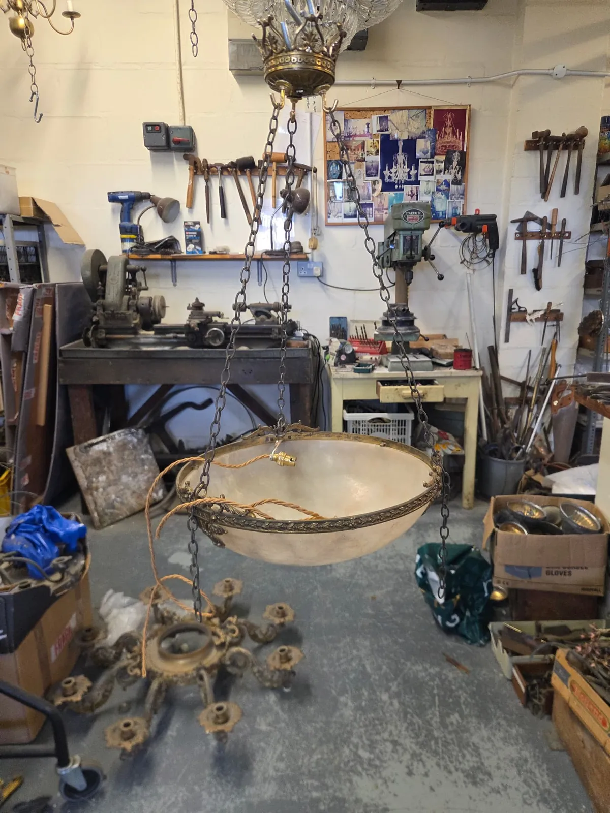 Alabaster bowl suspended above its ornate cast metal base in the workshop, with new cable still loose before the three-light wiring is completed.
