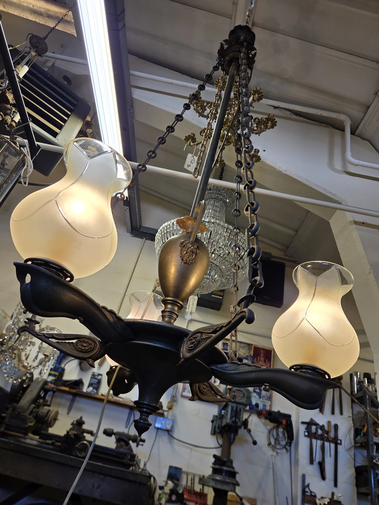 Underside view of a restored antique gasolier with illuminated colza glass shades and decorative metalwork.