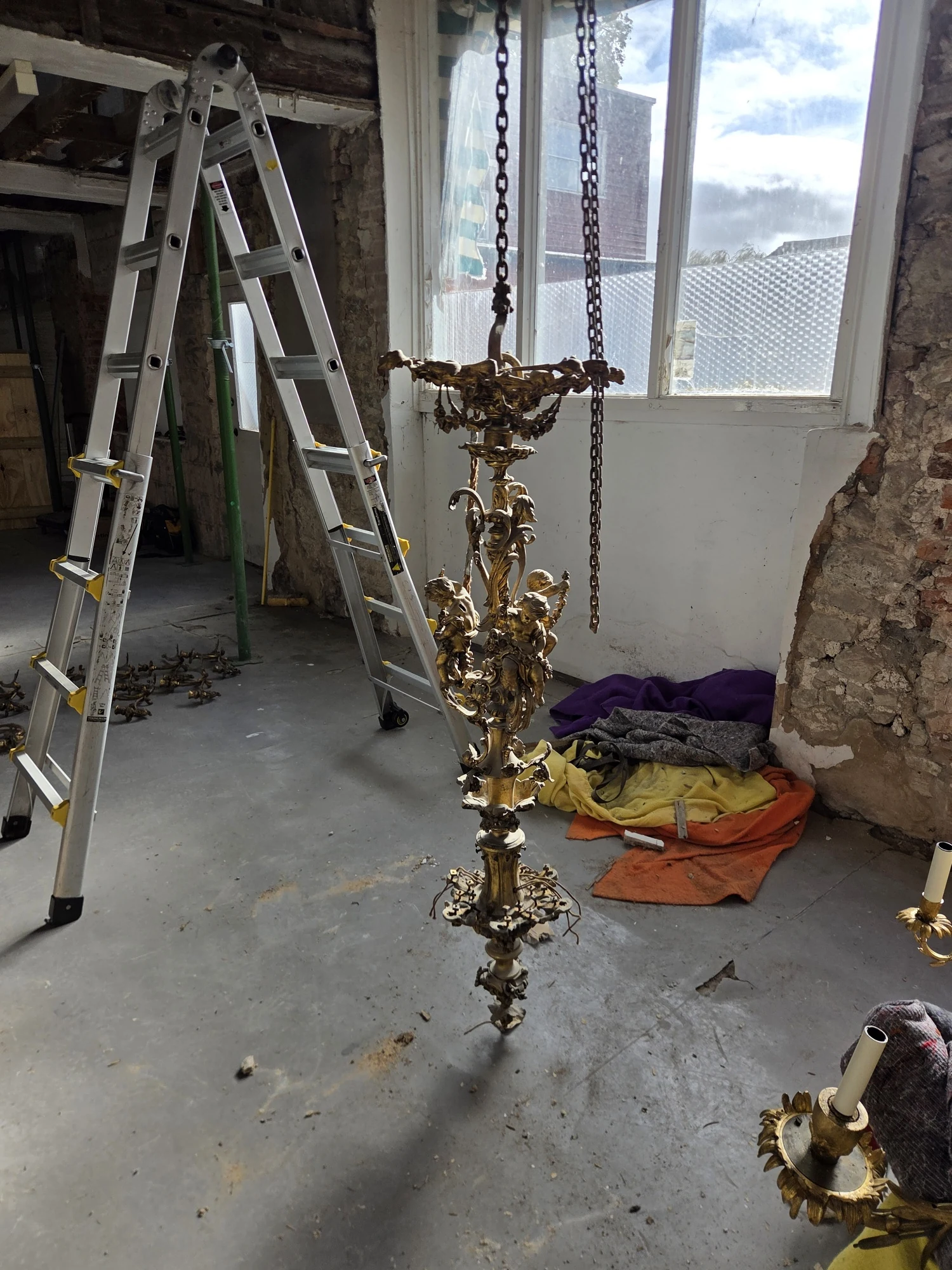 The tall gilt central stem hanging alone from its chains after all the arms were removed.
