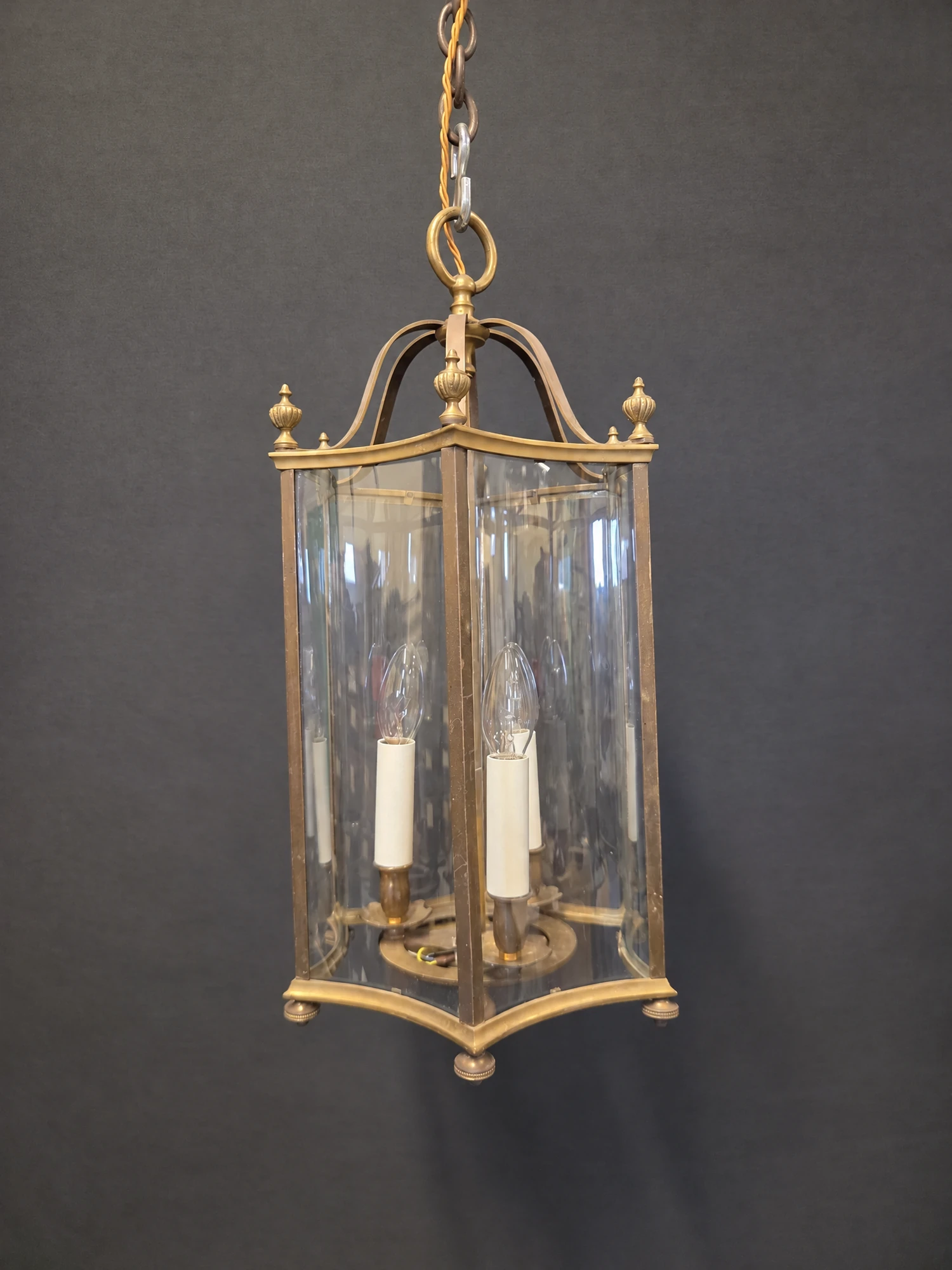 Hexagonal brass lantern with curved glass panels and three candle lights, shown in full hanging from its chain