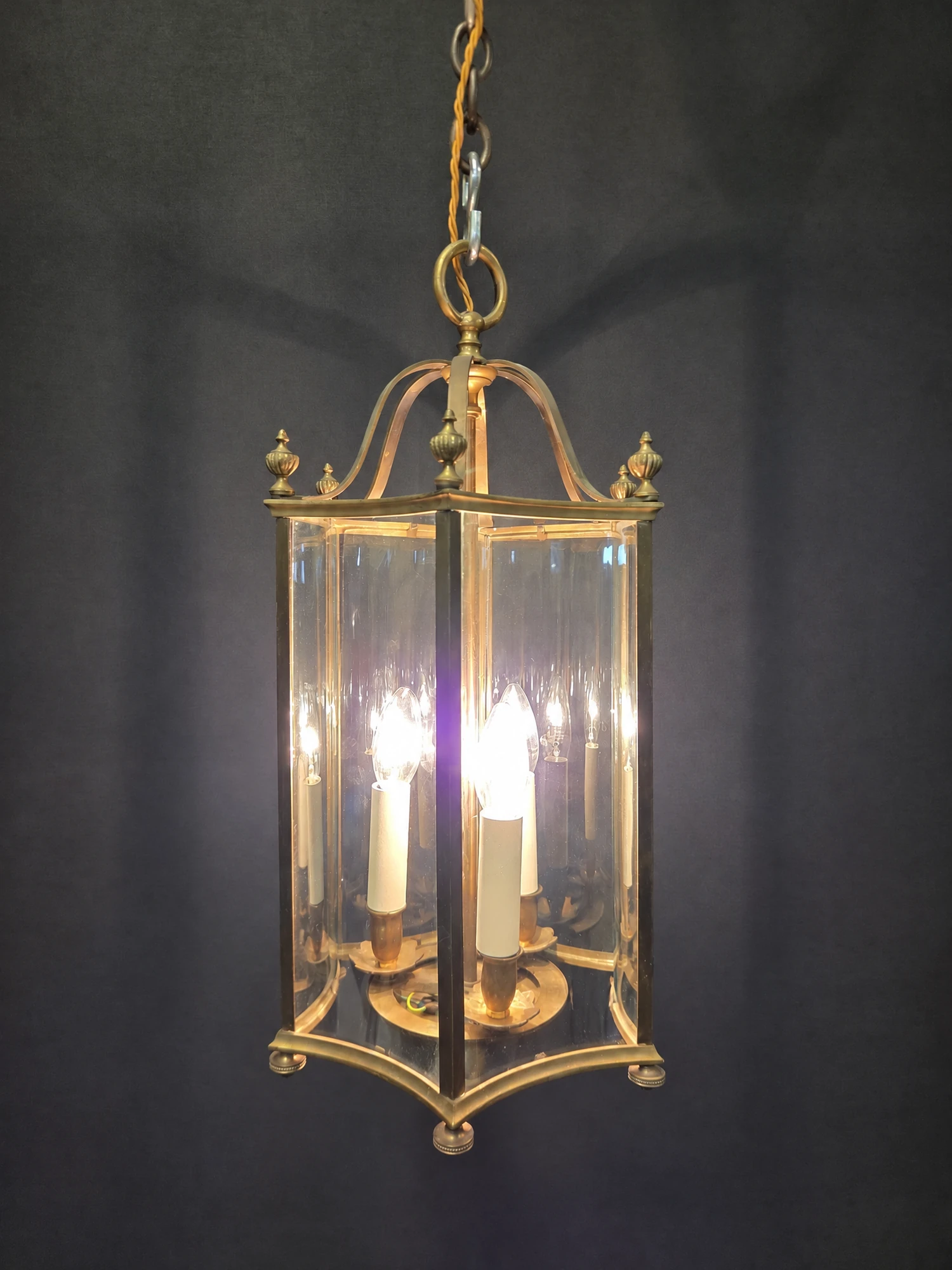 Hexagonal brass lantern illuminated, shown in full with its three lights lit behind the curved glass