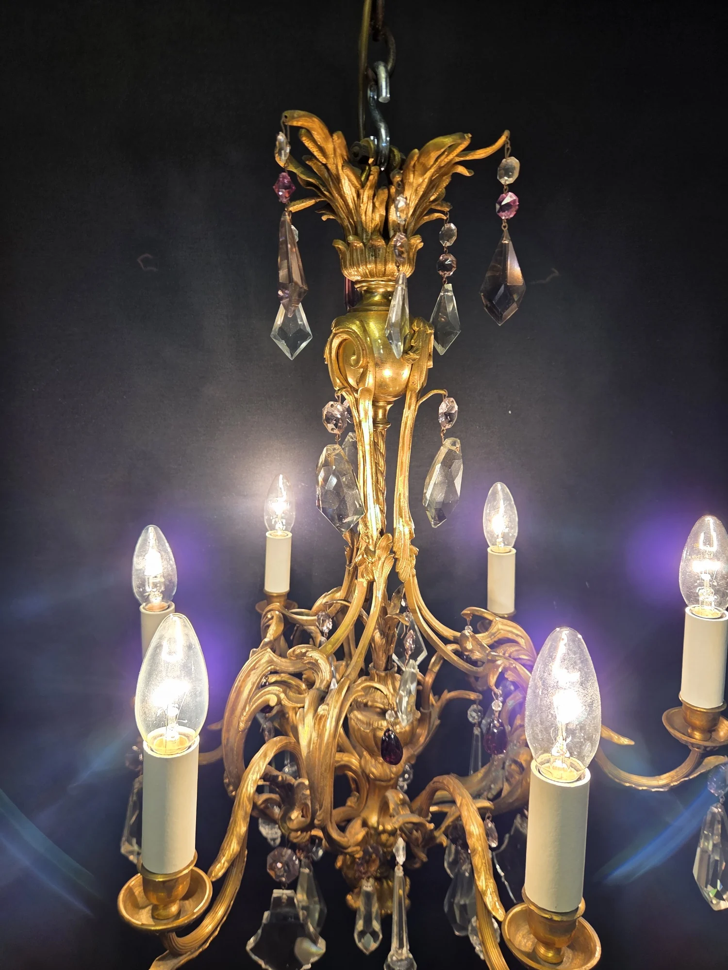 Illuminated French ormolu chandelier viewed from below, showing the scrolling frame and lit candle sleeves