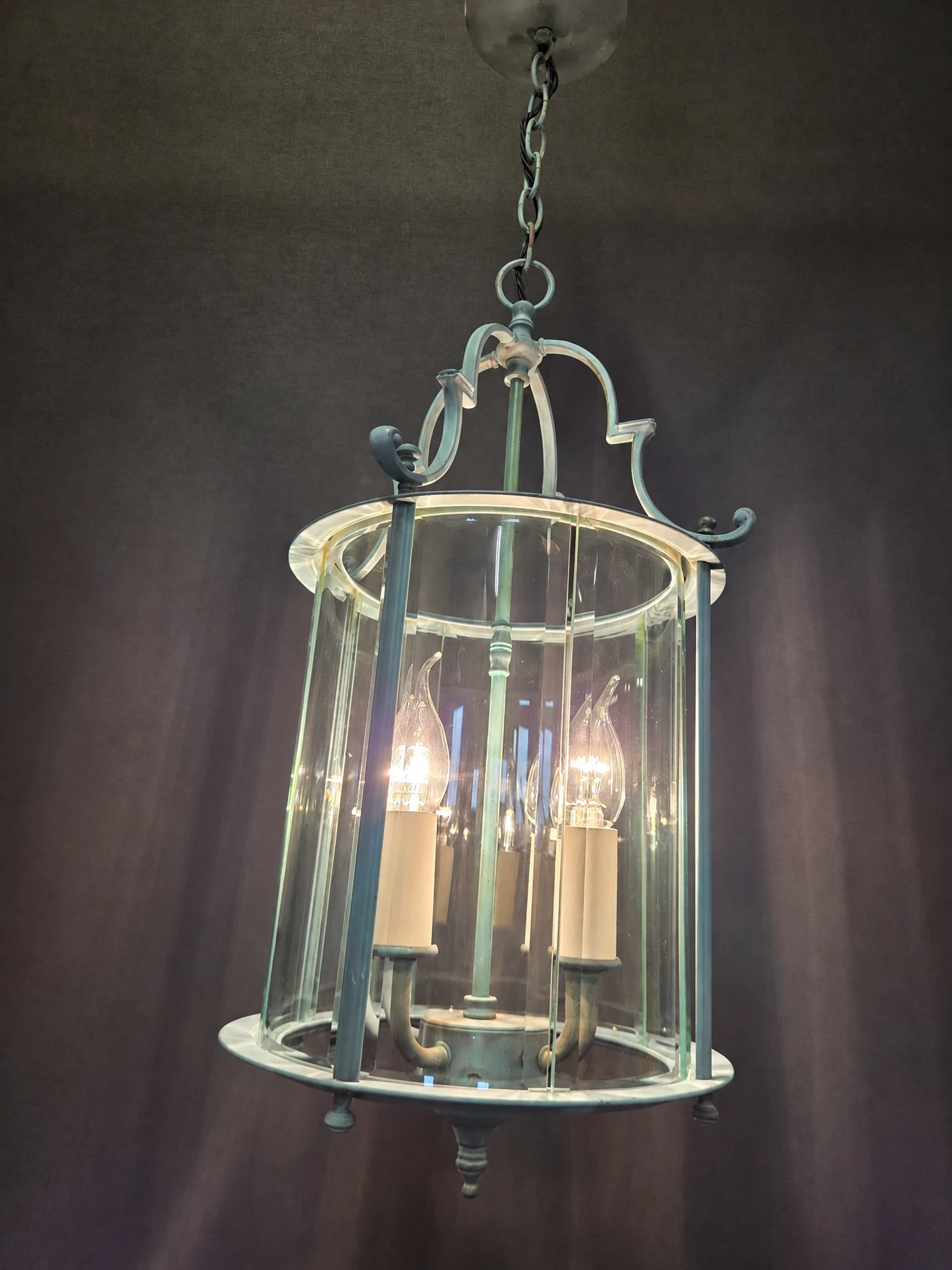 Illuminated round green lantern viewed at an angle, showing the curved bevelled glass panels and scrolled frame