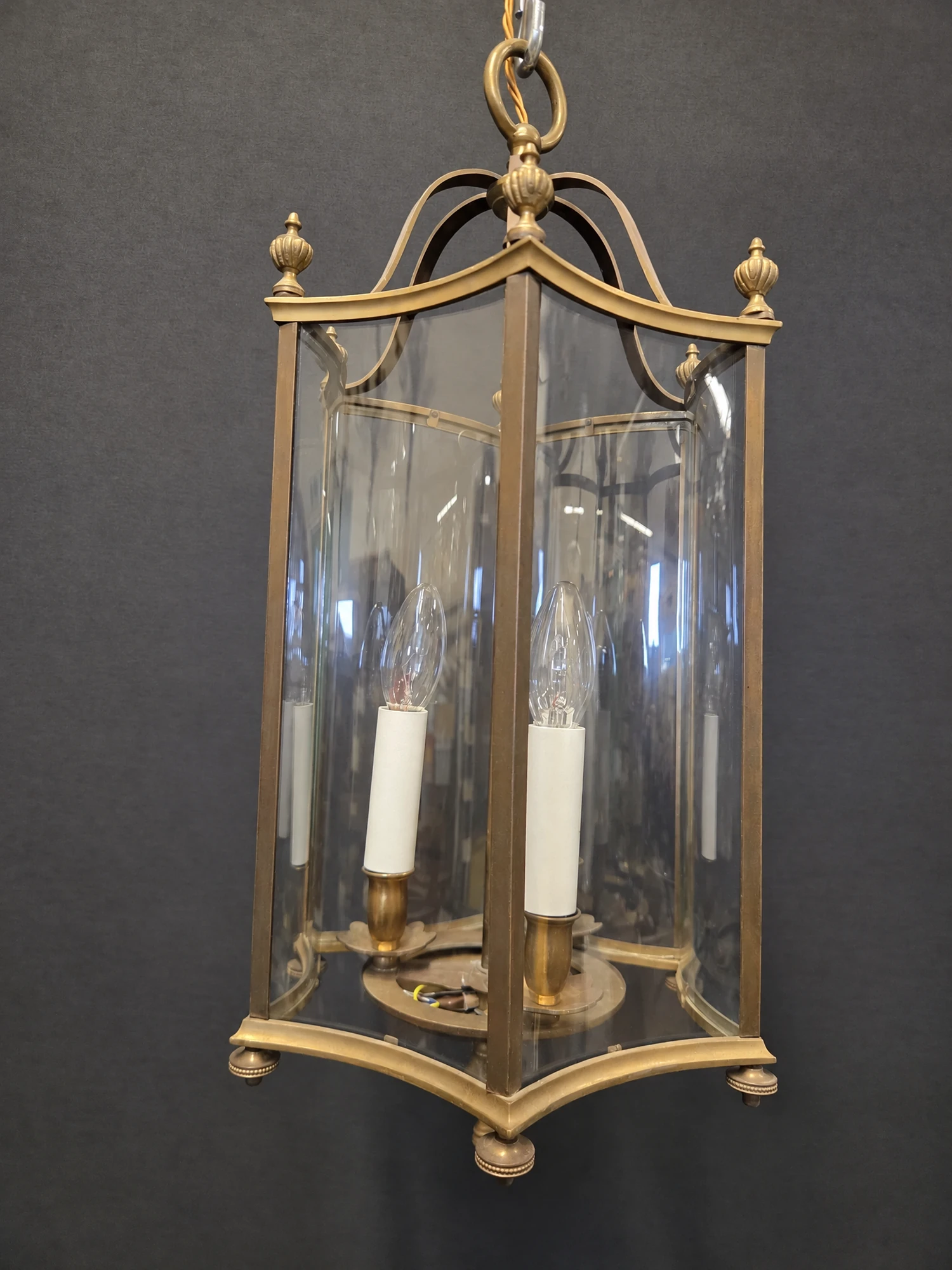 Closer full view of the hexagonal brass lantern showing the curved glass panels, finials and three candle sleeves