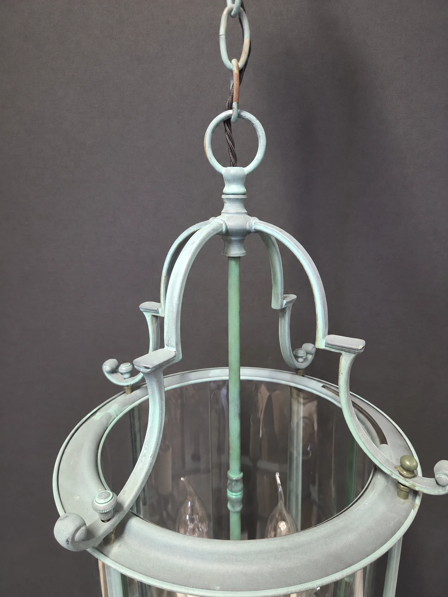 Close-up of the top of the round green lantern showing the suspension loop, scrolled ribs and central stem