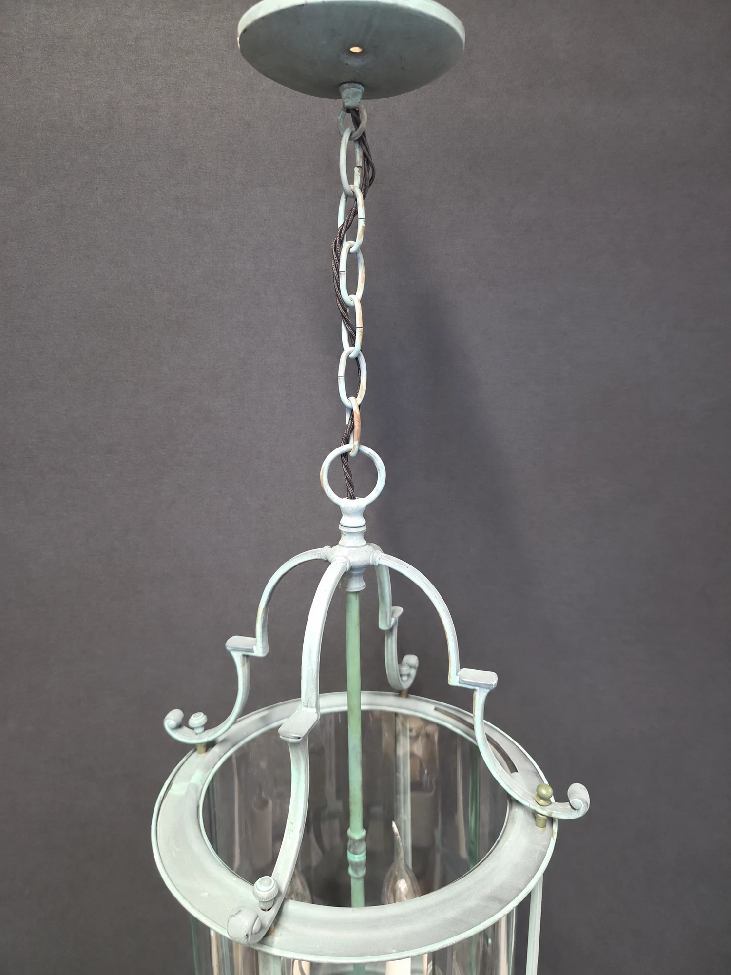 Close-up of the chain and ceiling rose of the round green lantern with the top of the frame beneath