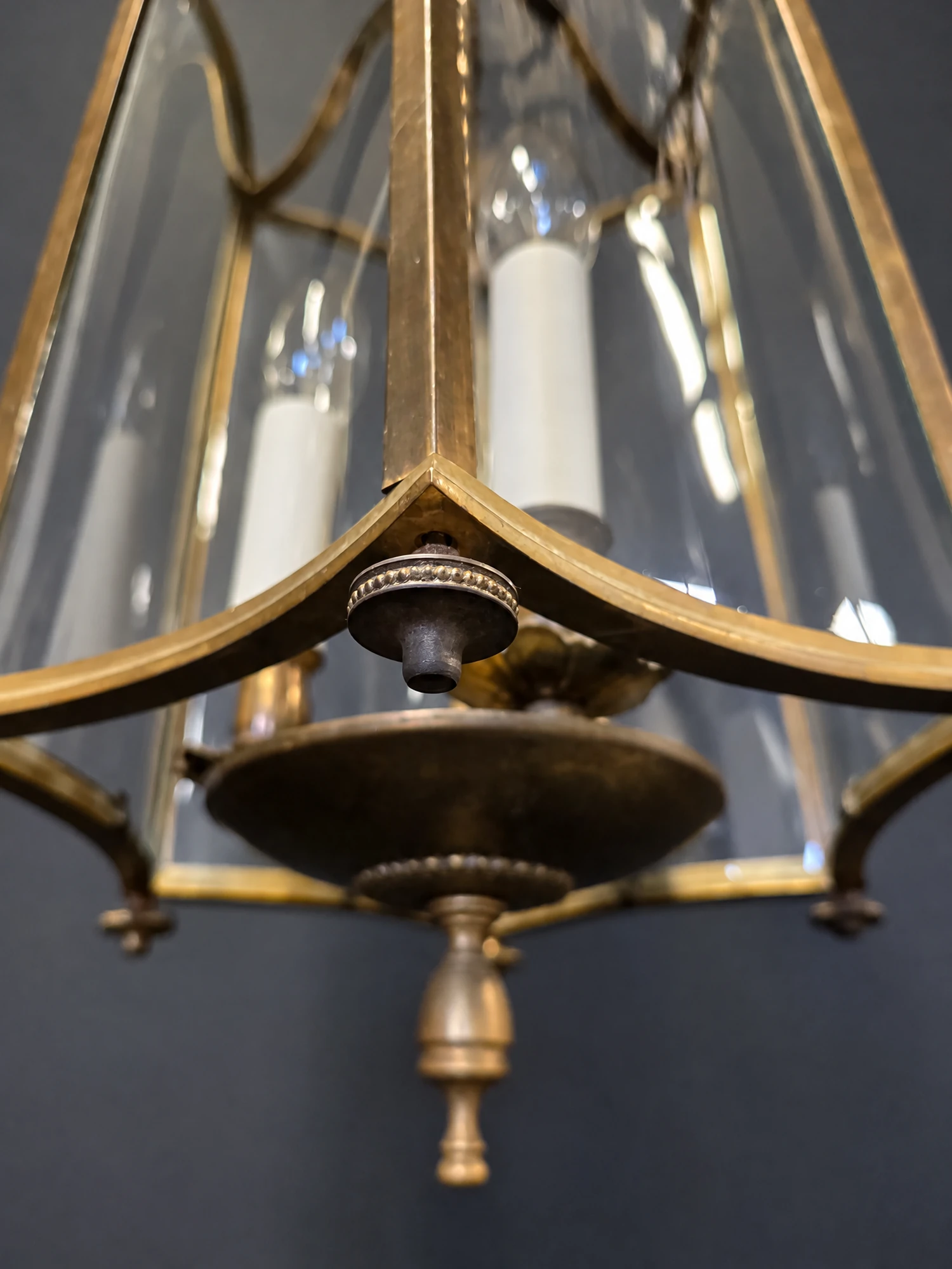Close-up of the lower corner of the brass frame, curved glass panel and turned finial beneath
