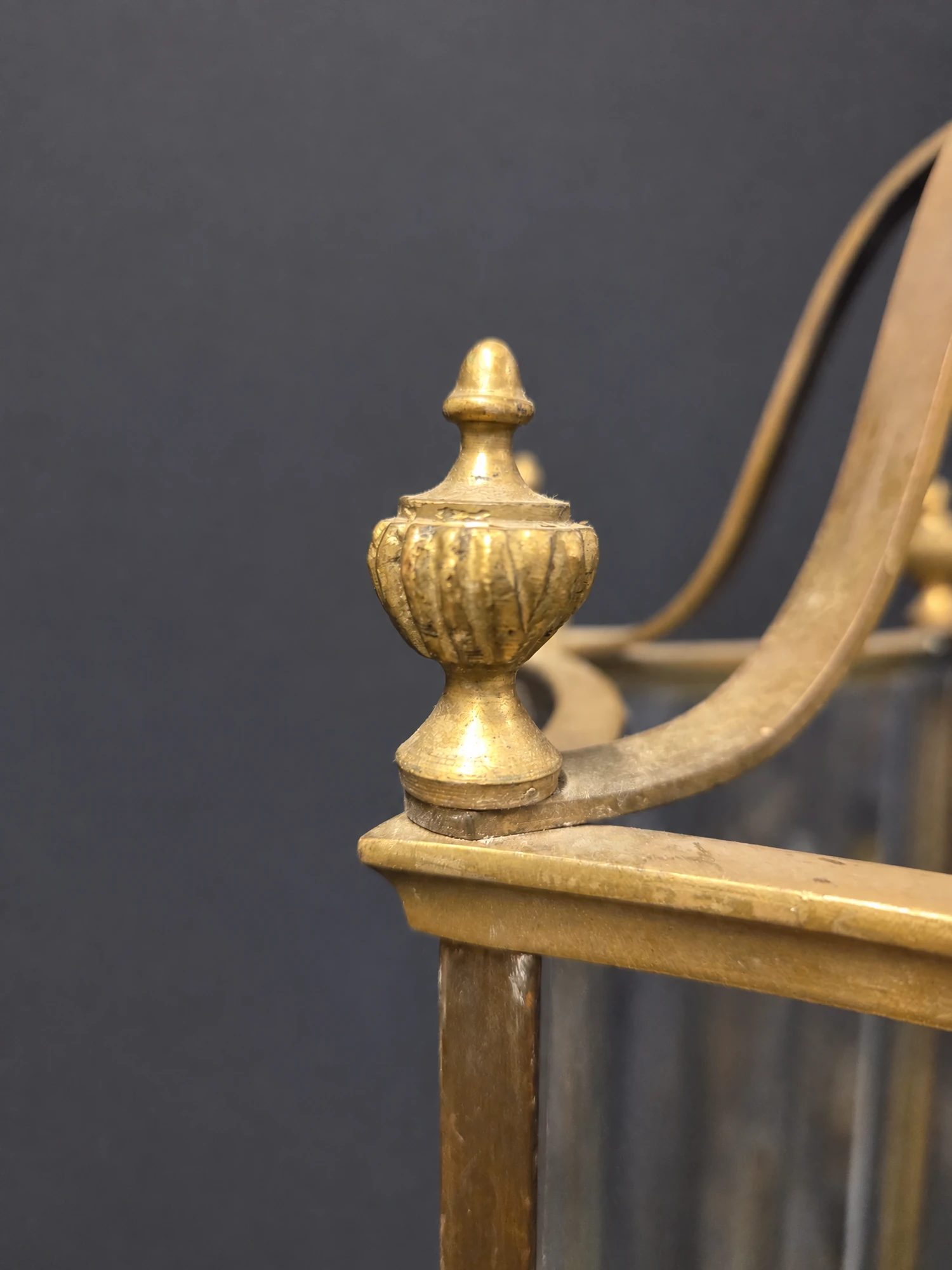 Close-up of a brass urn finial and scrolled top bar at the corner of the lantern frame