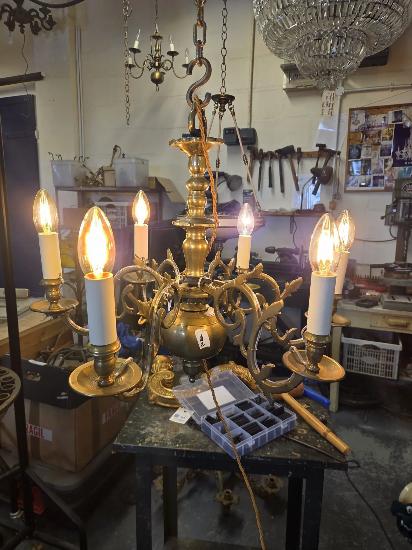 Full view of the six-arm brass chandelier lit during workshop testing