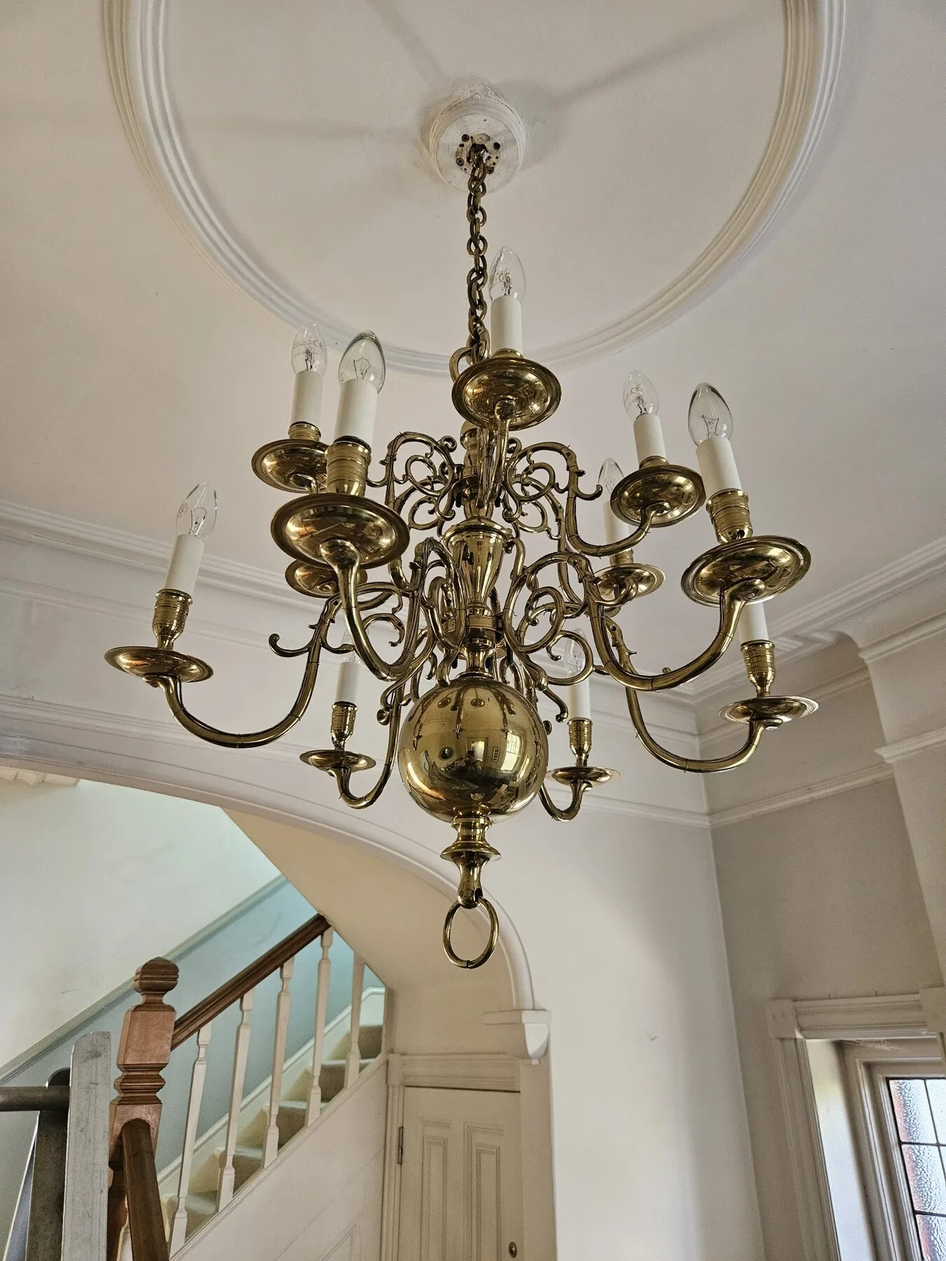 Dutch brass chandelier hanging from the new fixing beneath a circular plaster ceiling rose in South West London