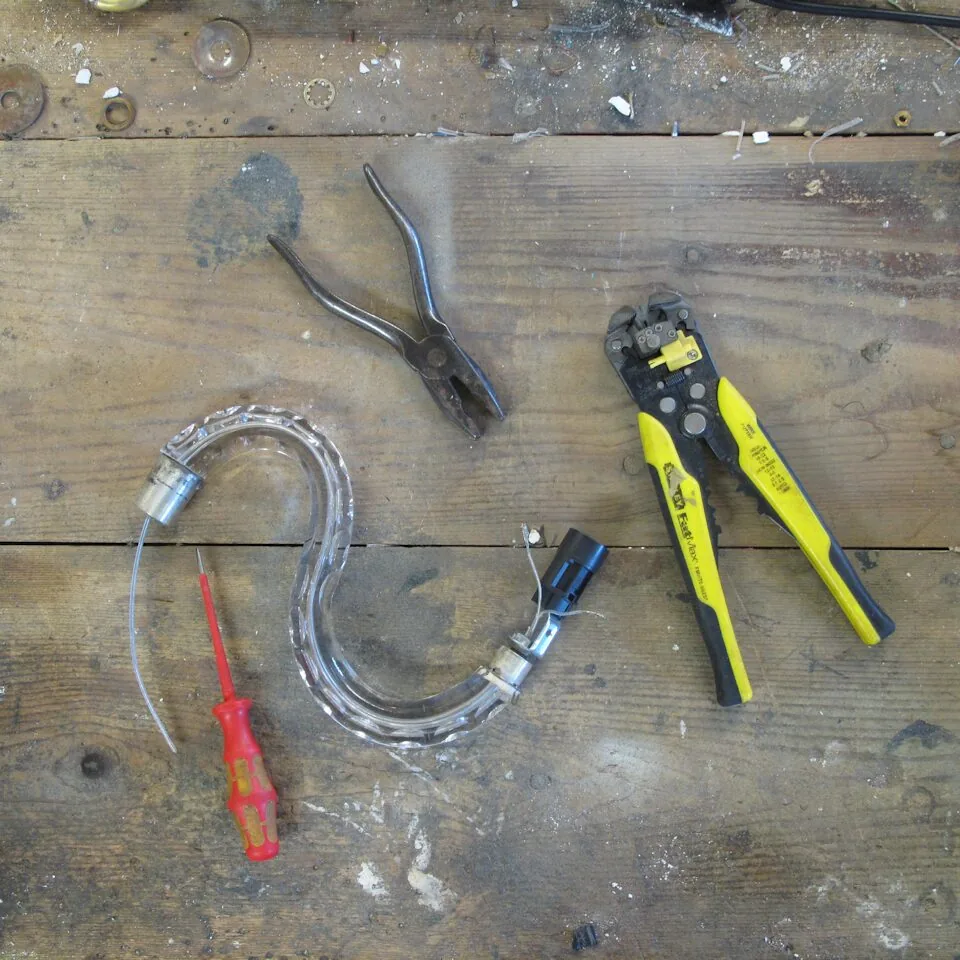 Workshop bench with chandelier arm, screwdriver, pliers and wire strippers ready for rewiring