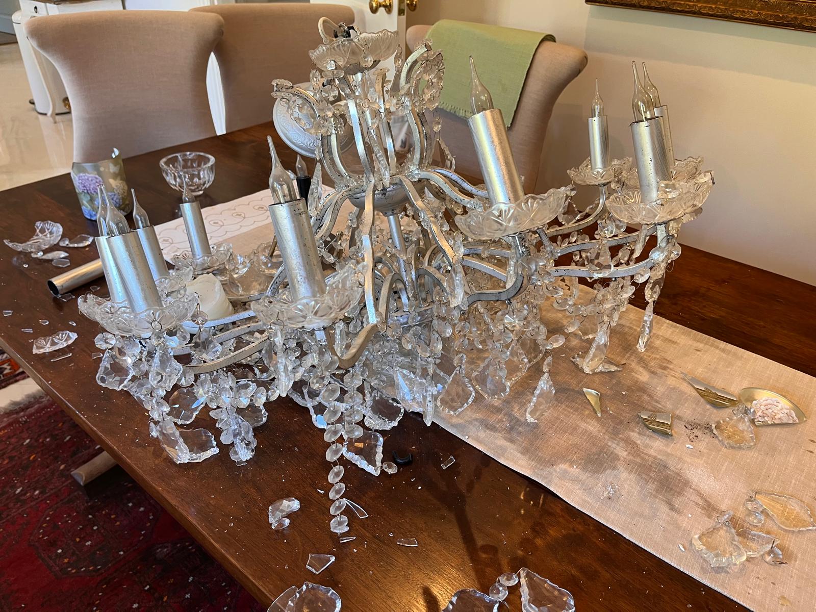 The chandelier on the dining table after falling from the ceiling, with broken glass around it.