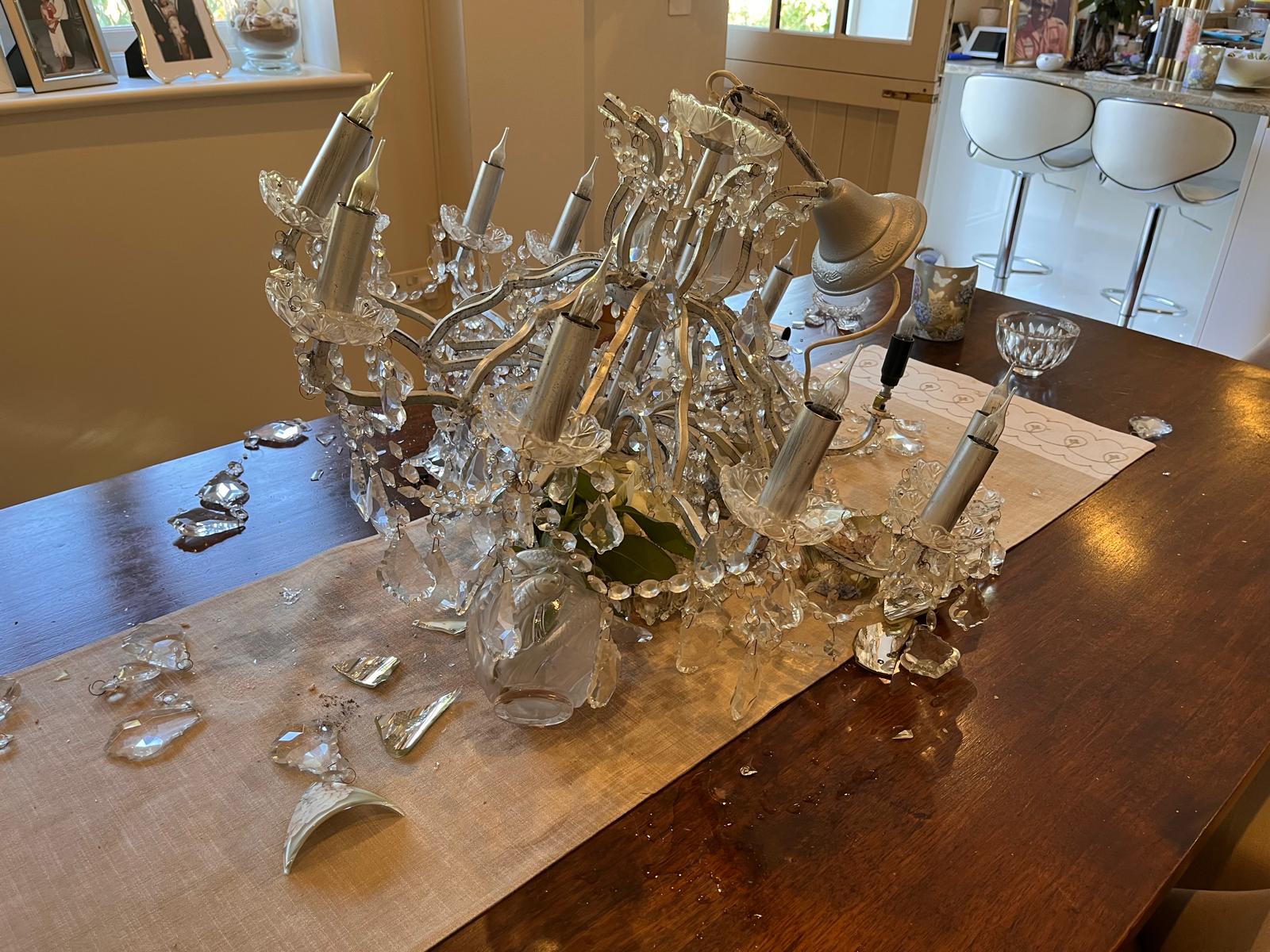 A further view of the fallen chandelier on the dining table showing damaged arms and glass.