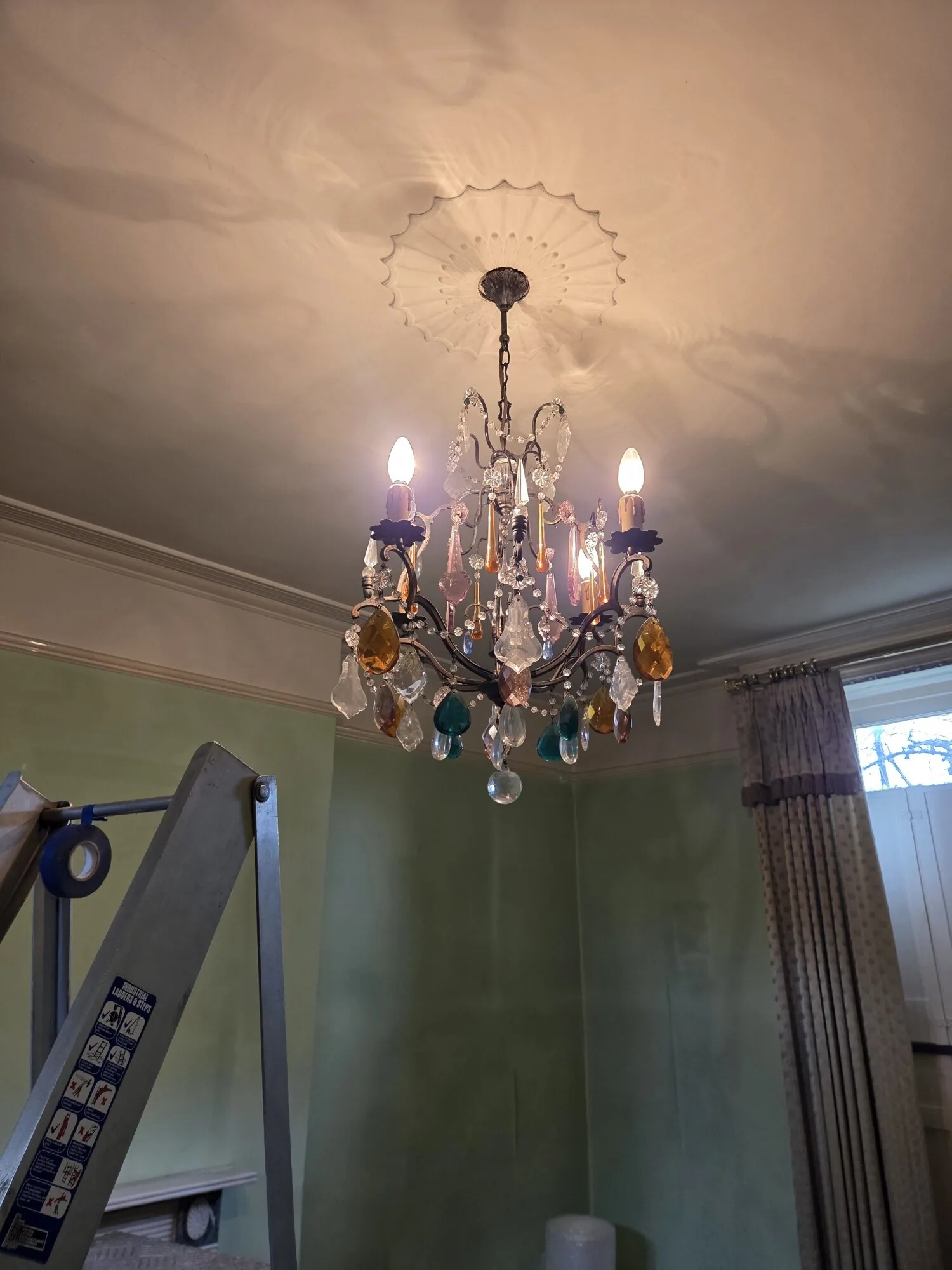 Antique crystal chandelier being cleaned in situ on a ladder